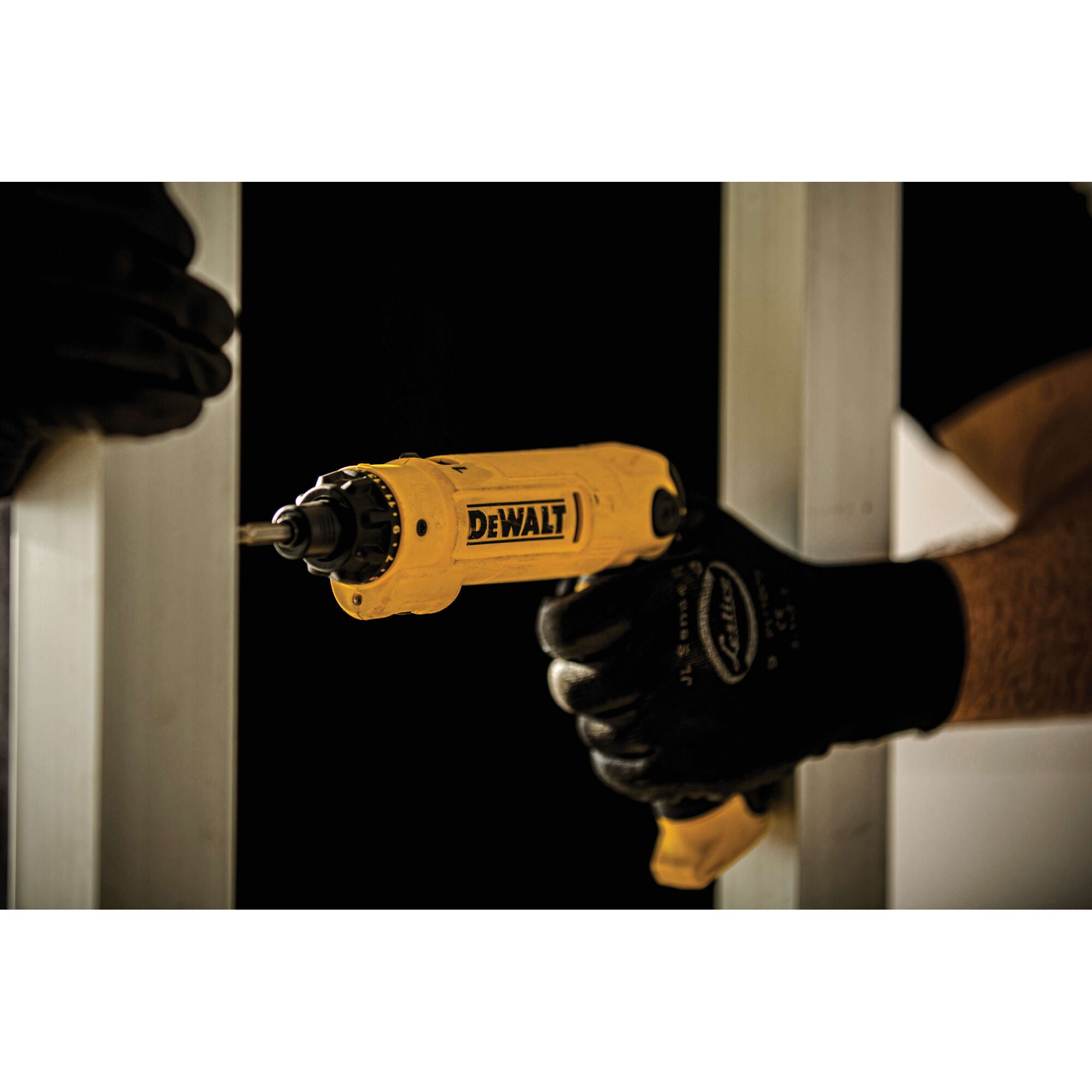 A person wearing black gloves is using a yellow DEWALT electric screwdriver to fasten a screw into a metal frame.