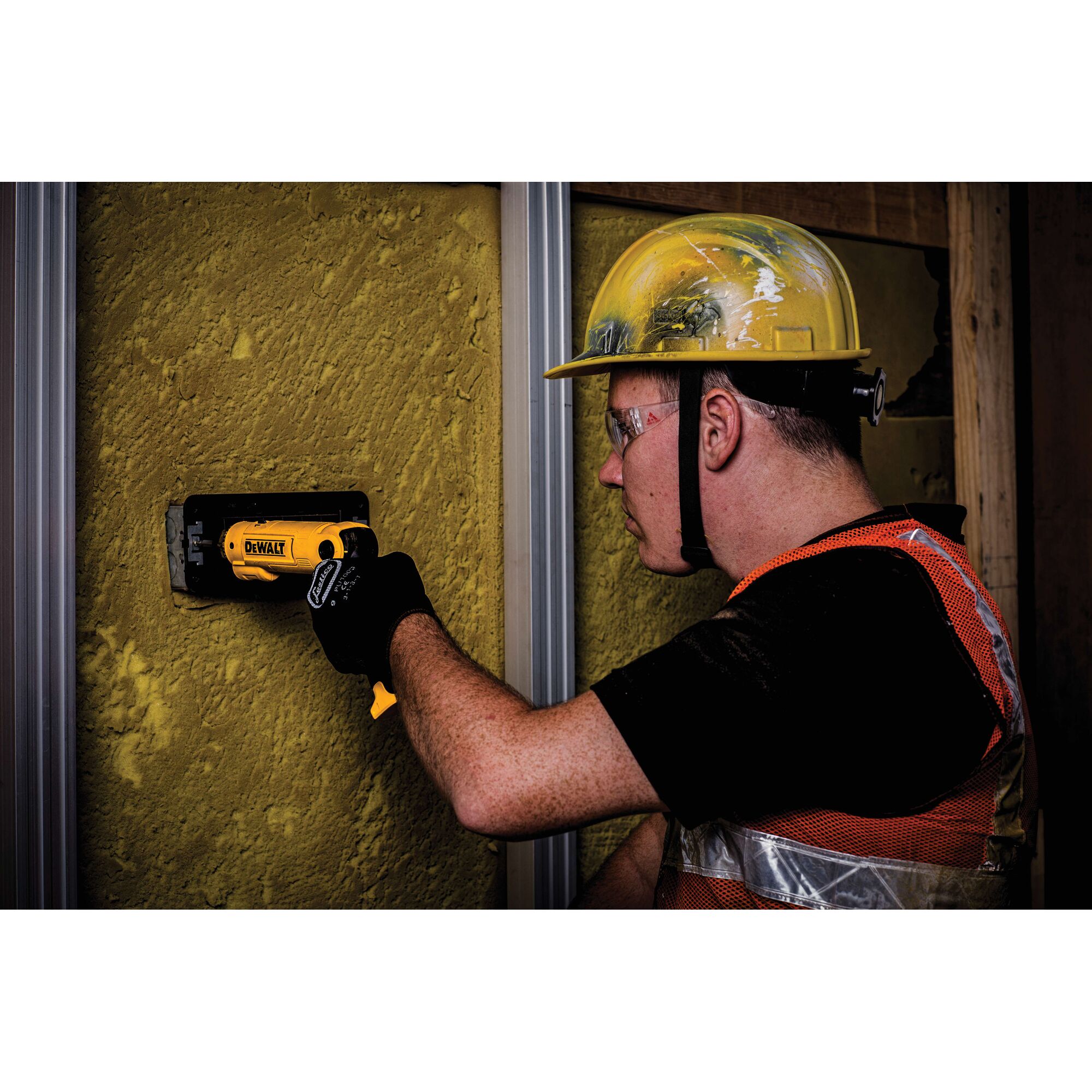 A worker wearing a yellow hard hat and safety vest uses a DEWALT DCF008 tool to work on a yellow surface wall at a construction site. The worker's face is blurred for privacy.