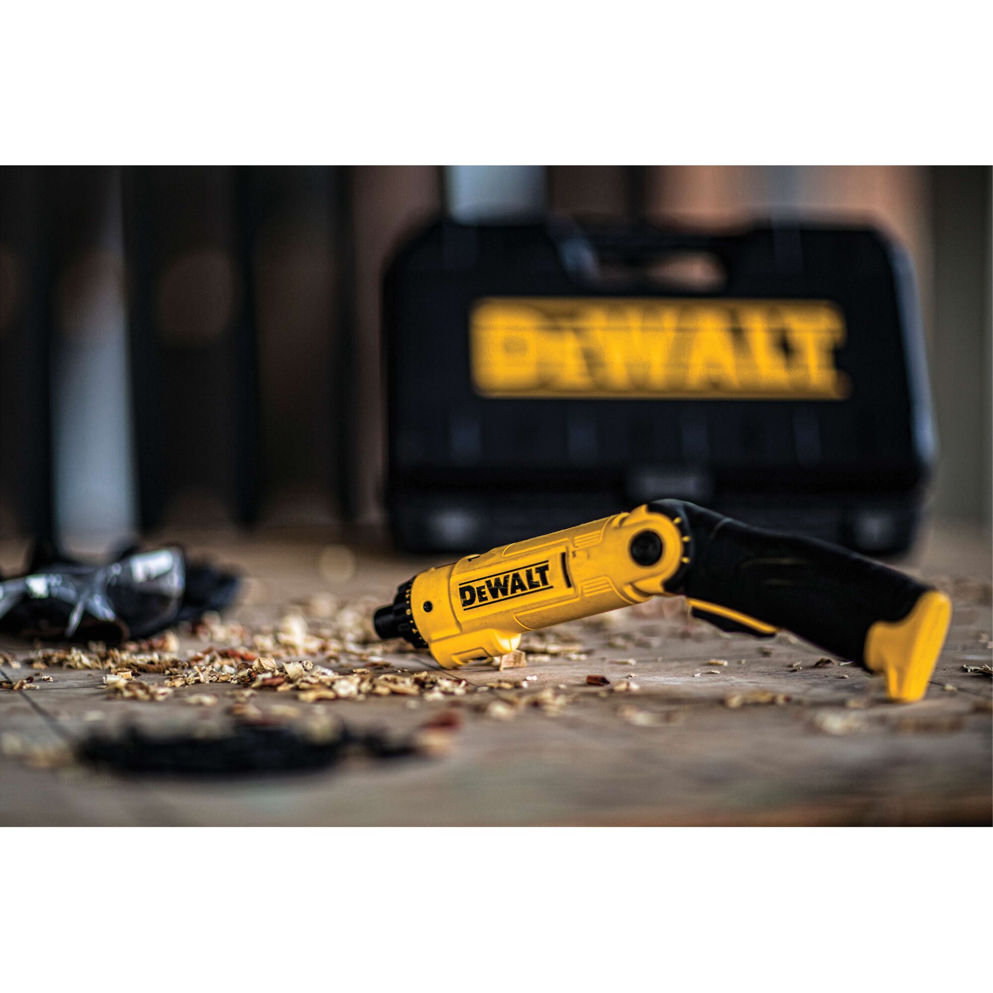 A DEWALT yellow and black cordless screwdriver (model DCF008) lies on a wooden surface with wood shavings around it, with a DEWALT branded carrying case in the blurred background.
