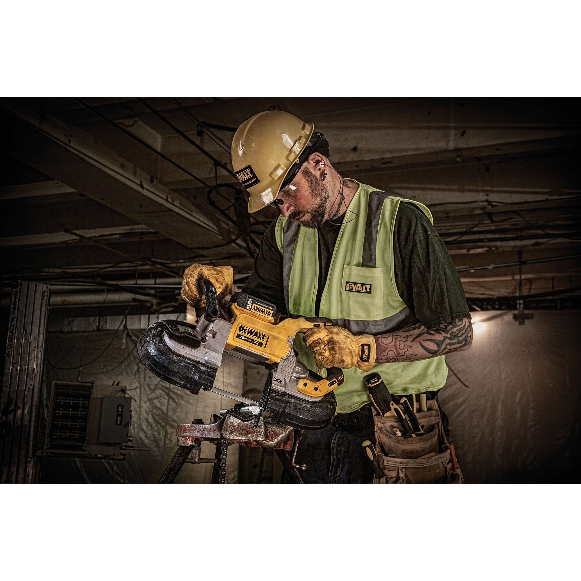 A worker wearing a yellow hard hat, safety vest, and gloves is using a DEWALT DCS374P2 portable band saw on a construction site. The worker's face is blurred for privacy.
