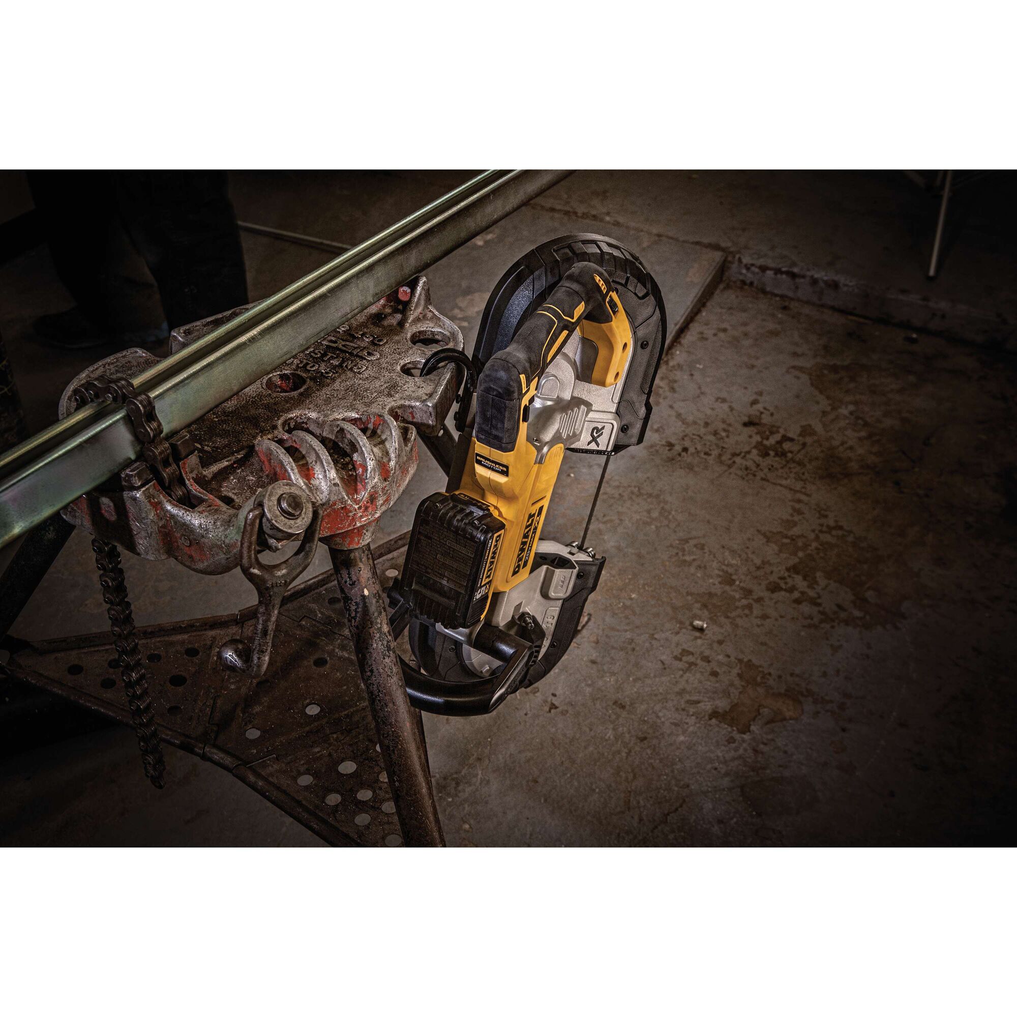 A DEWALT cordless band saw is shown cutting a metal pipe held in a clamp in a workshop setting.