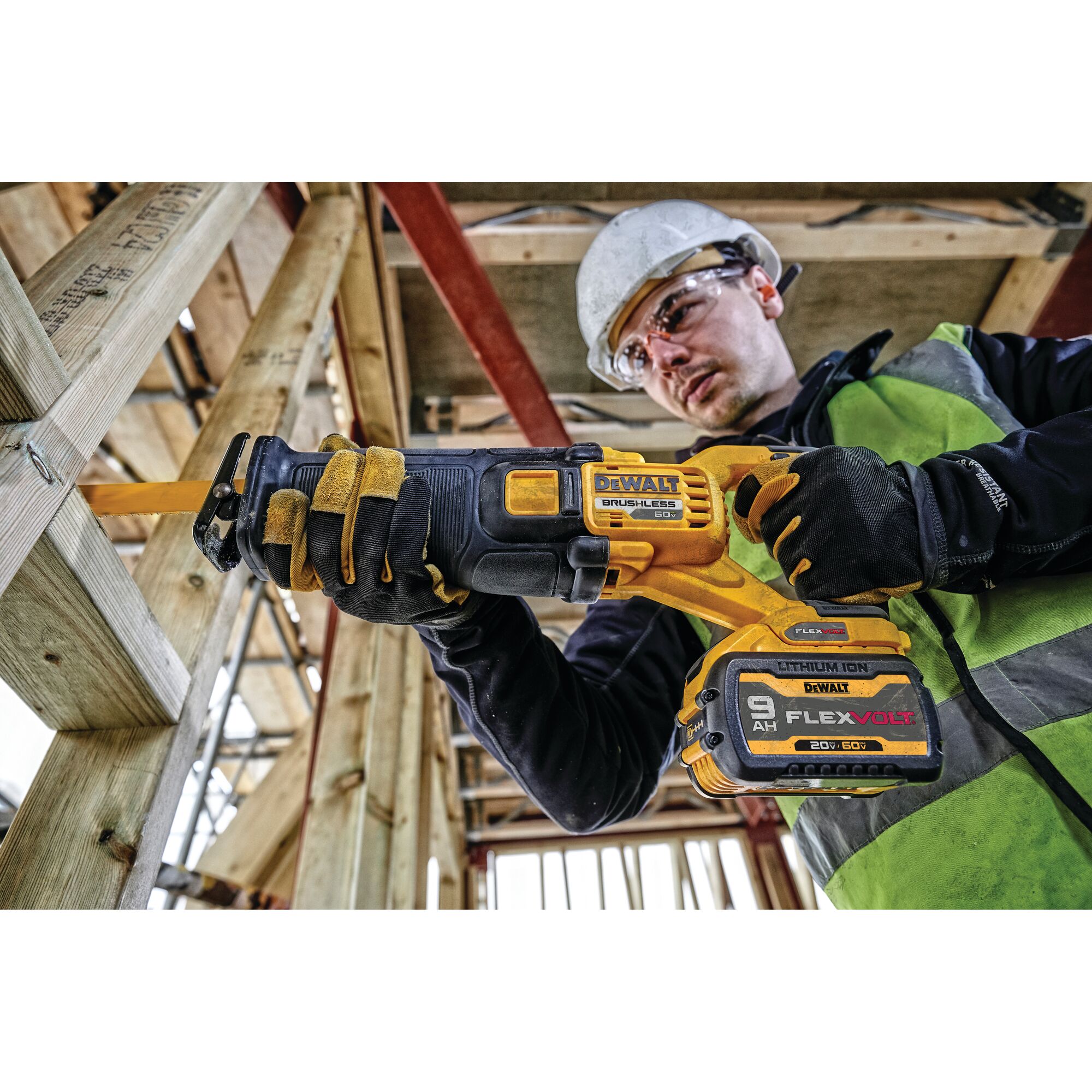 A person wearing a safety helmet and vest operates a DEWALT DCS389X2 20V/60V brushless reciprocating saw with a FLEXVOLT lithium-ion battery, cutting through wooden beams at a construction site.