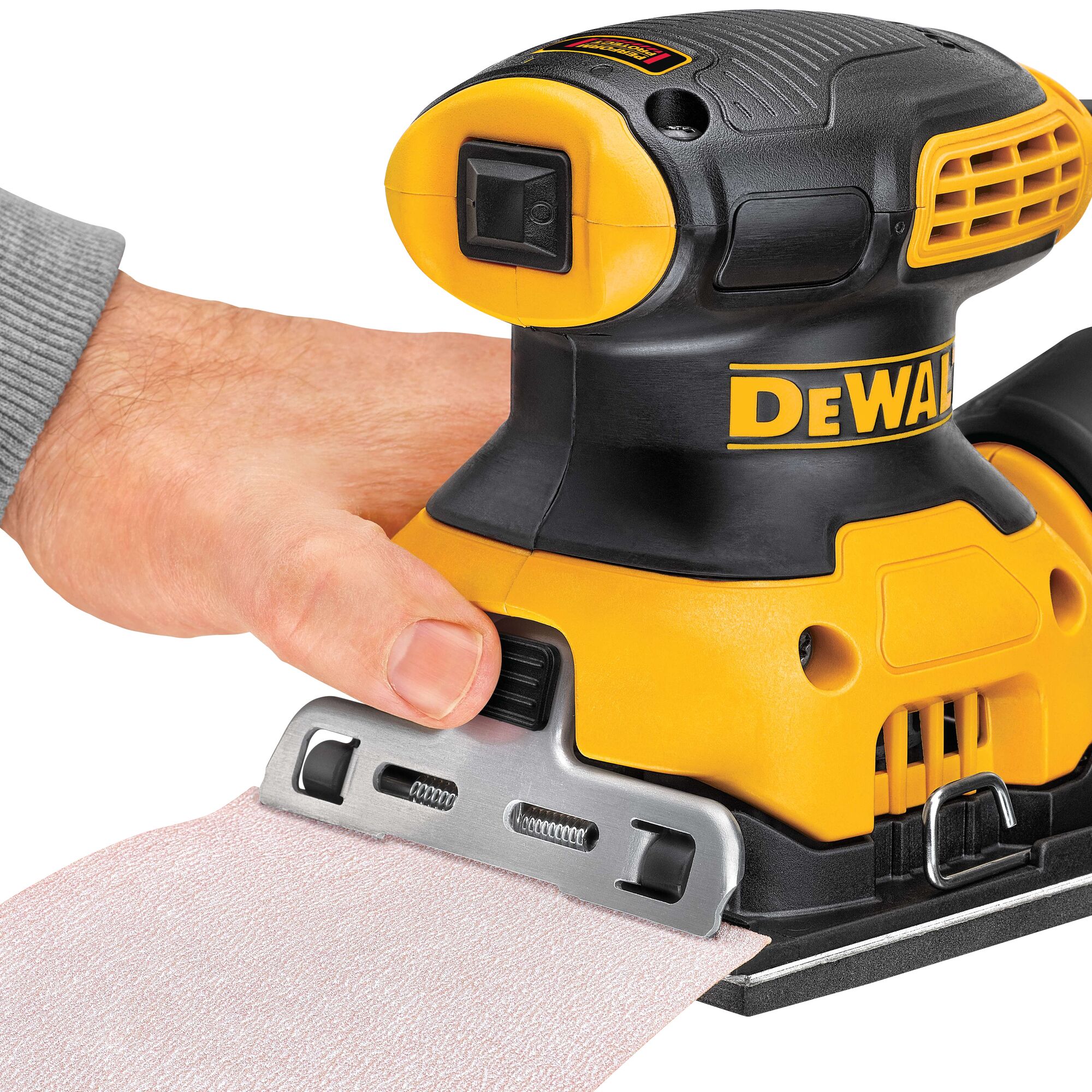 Close-up of a DEWALT electric sander, with a person's hand operating the tool and loading sandpaper onto the base.