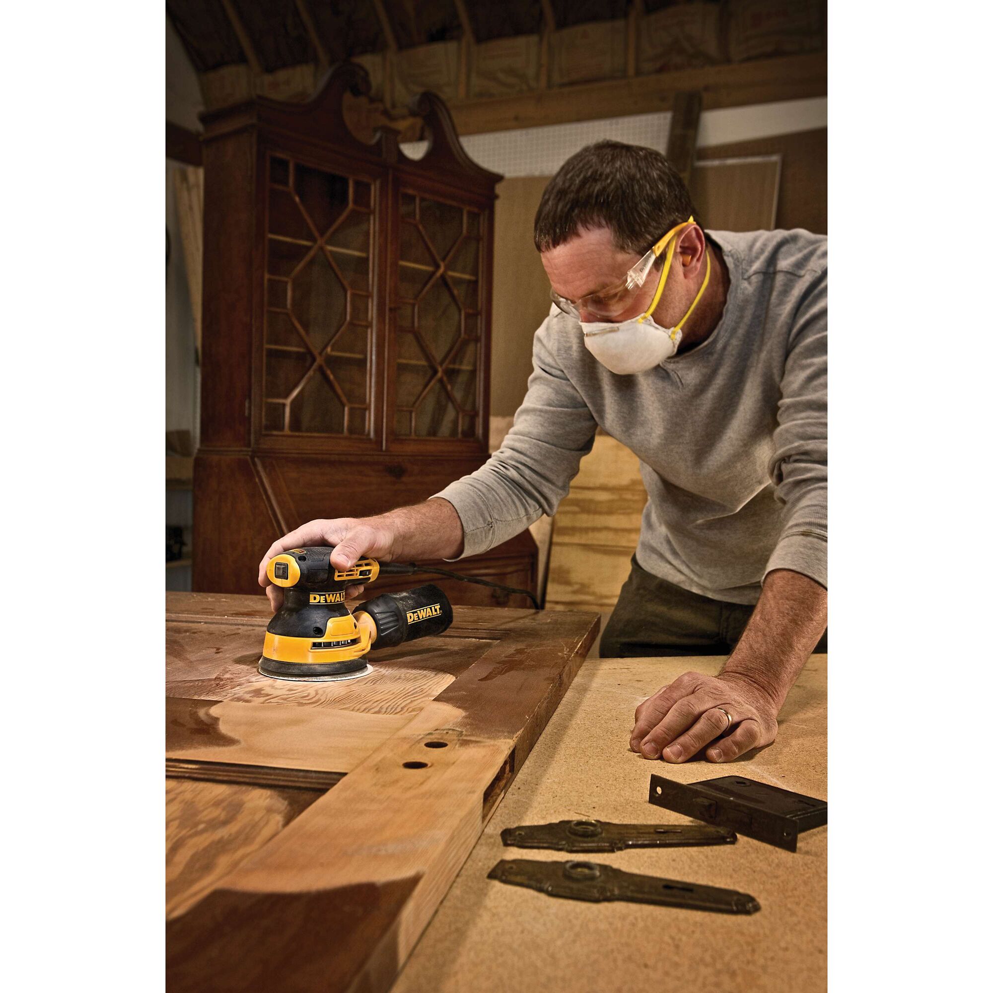 5 inch variable speed random orbit sander in action in use to sand a wooden sheet by a worker.